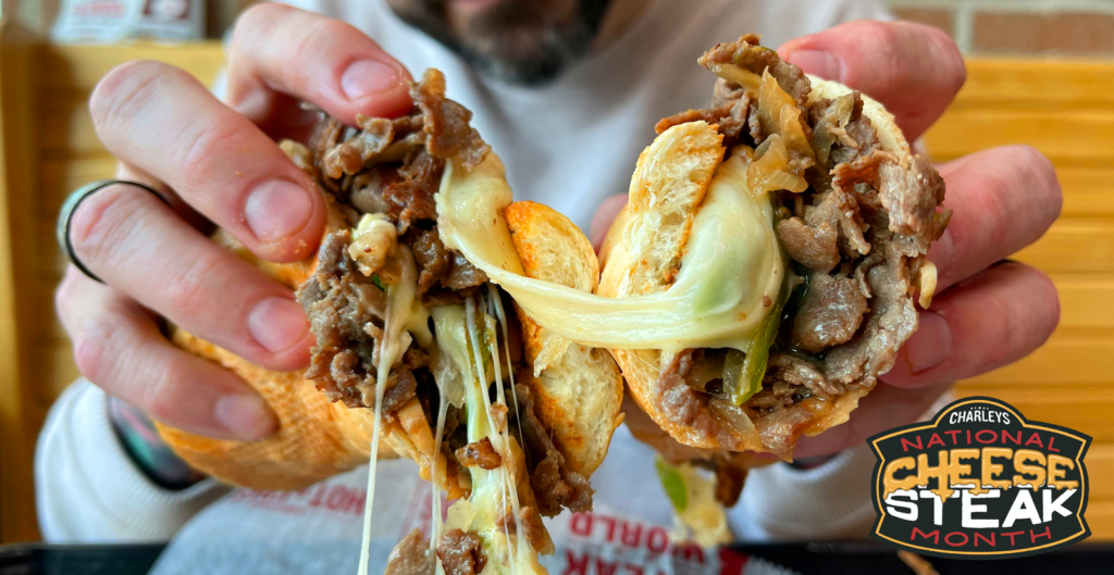 A person holding a cheesy cheesesteak from Charleys with a logo in the corner that says National Cheesesteak Month. Cheese Steak, cheesesteaks.